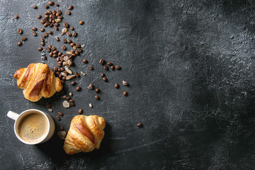 Fresh baked traditional croissants and mug of espresso coffee, coffee beans, sugar over black texture background. Top view, copy space