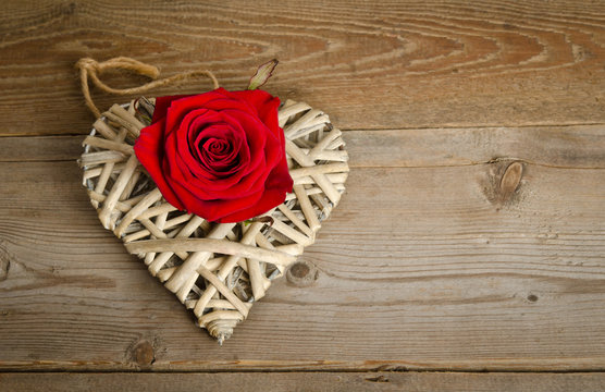 wicker heart handmade with bud of red rose lying from left side on a wooden base.top view