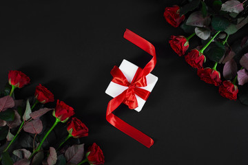Red roses, ring and gift box on black background