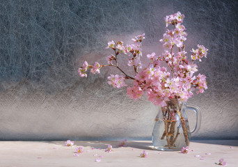 Pink cherry blossoms in vase on wooden table in the sunlight.