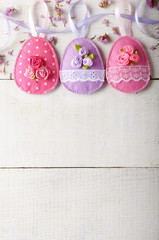 Handmade patchwork pink and lilac felt easter eggs on white wooden table