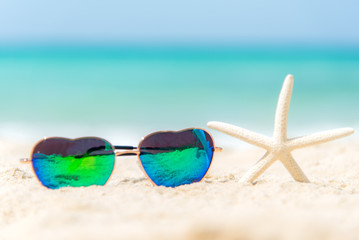 Fototapeta na wymiar Summer Fashion heat shape sunglasses on sea beach under clear blue sky. Summer holiday relax background, copy space.