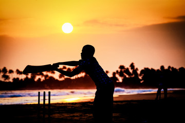 boy playing cricket at sunset on tropical beach in Sri Lanka