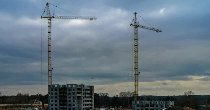 Time lapse of silhouettes of cranes working on a construction site of a multi-storey building in a cloudy evening
