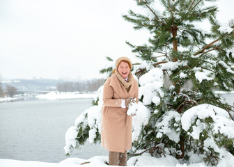 Happy woman outdoors playing in the snow against a background of spruce.