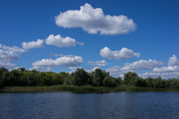 Clouds near the river bank. Fluffy clouds over the river. Beautiful summer landscape.