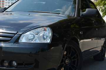 Fototapeta na wymiar Black shiny car. The headlight and the side of the car. Car on black cast wheels.