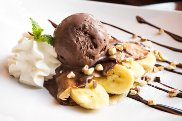 Crepe with banana and chocolate icecream. French dessert. Served on white plate with whipped cream.