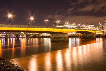 London Bridge illuminated in yellow light at Night.  Long exposure creating a smooth, glassy effect on the Thames River.