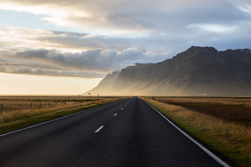Photo of a long stretch of road with a beautiful breathtaking scenery of the mountains and the sunset