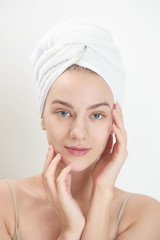 Skin care. Young woman on white background with towel on head touching her clean skin on the face