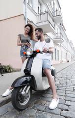 Obraz na płótnie Canvas Young happy couple riding scooter together smiling