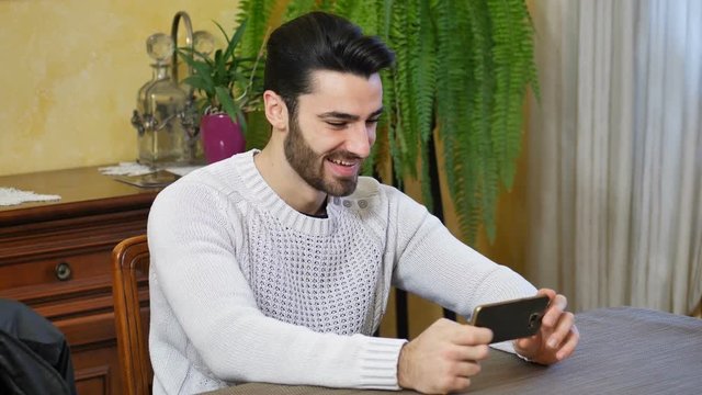Attractive happy young man typing on cell phone, indoor shot in house living room
