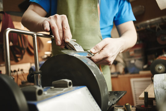 Making of a knife. Master sharpens a blade on the machine closeup in the Studio