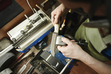 Making of a knife. Master sharpens a blade on the machine closeup in the Studio