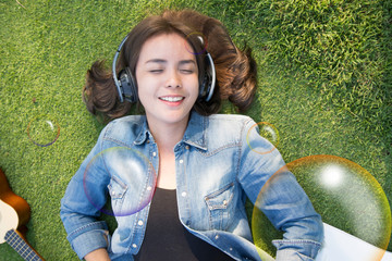 Relaxing women listening music laying down on the grass with headphone and smile bubble foreground, Top view