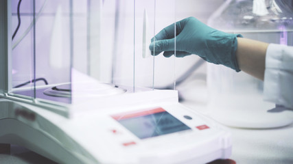 Scientist s hand in a green glove is putting liquid at electronic scales in a lab. Medium shot. Uni...