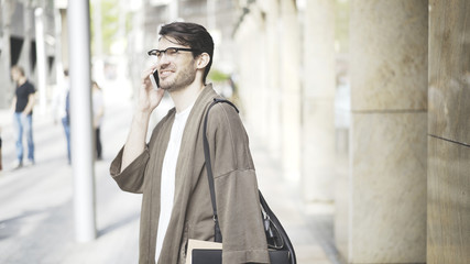 Side view of a handsome businessman walking towards camera and using a smart phone in the street.