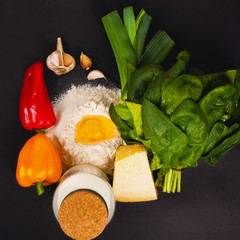 Vegetables, flour, eggs to cook quiche on a dark background, top view