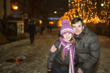 Happy father and daughter are walking around the night city during snowfall