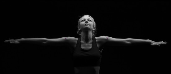 Fototapeta na wymiar Beautiful fit and healthy blond woman in black top in dark with arms stretched artistic conversion