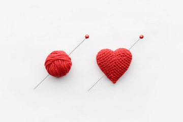 a knitted heart of red thread with an inserted knitting needle on a white background. and a hank of...