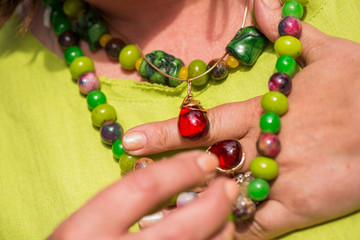 Woman wearing beautiful gemstone necklace and golden ring with amber. Jewelry made of coral, olivine and agate stones. Powerful energy of healing crystals