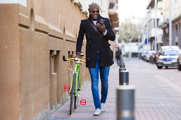 Handsome young man using mobile phone and fixed gear bicycle in the street.