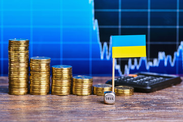 Downtrend of stacks of gold coins, flag of Ukraine, dice cube and calculator