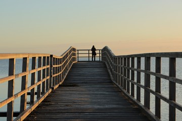 Obraz premium Kobieta stoi samotnie i samotnie na malowniczym molo nad Morzem Bałtyckim, Eckernförde, Schleswig-Holstein, Niemcy, Europa