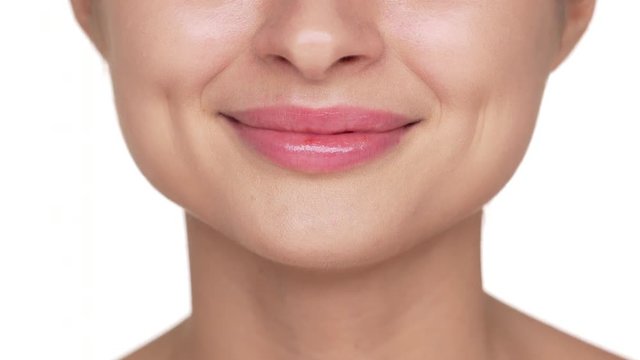 Macro shot of natural lips with pink lipgloss of beautiful young woman having clean healthy skin posing over white background. Facial expressions