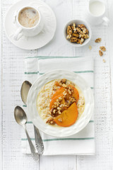 Oatmeal porridge with caramelized persimmon and walnuts in a light ceramic bowl on a white wooden background. Selective focus. Top view. Copy space.