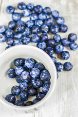 Juicy blueberries in a small white jar with scattered blueberries on the wooden table.