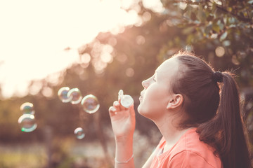 Beautiful young brunette girl blowing soap bubbles outdoor during lovely summer sunset