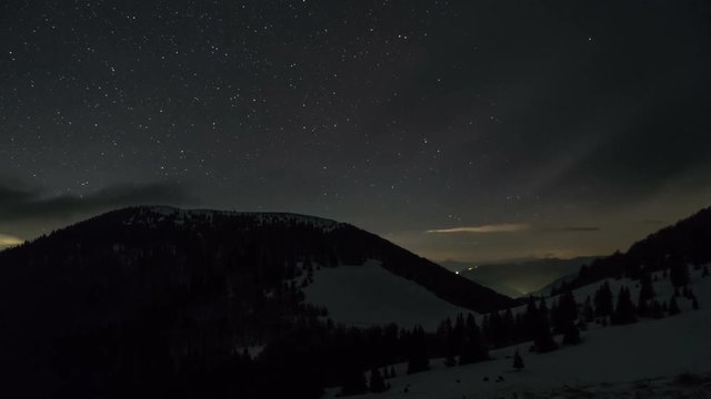 Stars and clouds moving in night sky over winter mountains. Dreamy astronomy time lapse