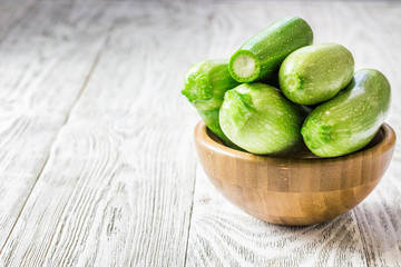 Fresh zucchini in a bowl and slices on white wooden background. Selective focus, copy space, close up.