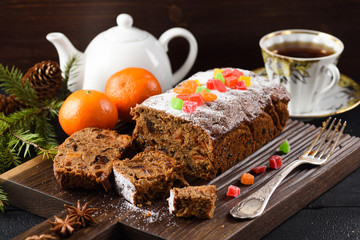 Delicious sliced fruit cake on wooden board served with tea and clementines