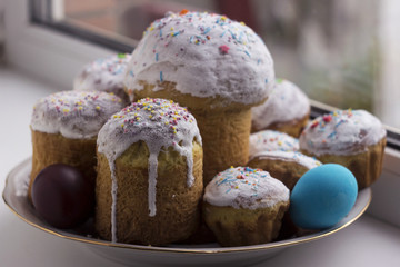 Easter cake with white icing and sprinkled with little candies on the plate on the window sill. A lot of cakes