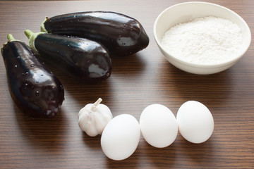 eggplant, eggs, flour, garlic on a wooden background