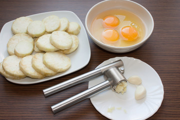 peeled and chopped eggplants, broken eggs, garlic press on a wooden background. Ingredients