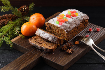 Traditional fruit cake for Christmas served on wooden board with clementines on black background