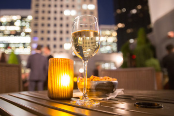 Glass of white wine and candle with evening view of city buildings