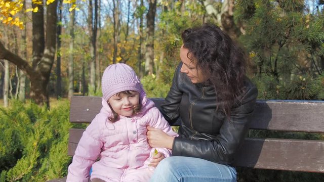 Happy mother with her daughter in the autumn park. A woman is talking with a child.