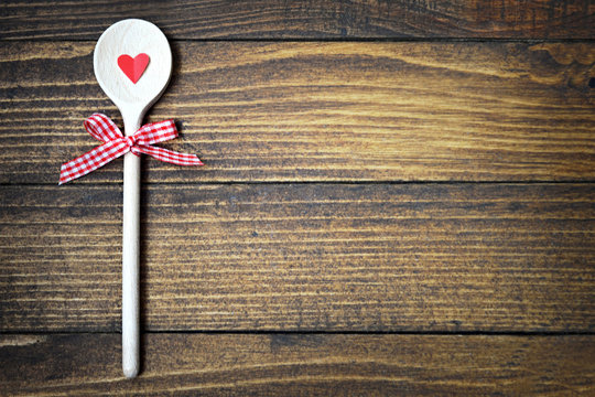 Valentine cooking background with copy space. Wooden spoon with red heart and bow on rustic wooden background 
