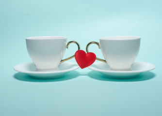 Two white cups and a red heart on Valentine's Day stand on a turquoise background. Valentine's day card