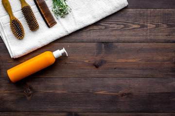 Product's for daily hair care. Comb, shampoo, towel on dark wooden background top view copyspace