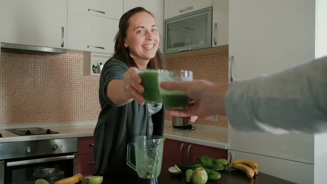 Healthy cheers. Young woman making a green vegetable and fruit smoothie on a blender. 
