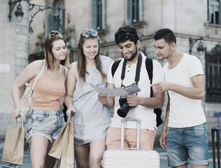 Four cheerful traveling young people with map