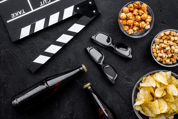 Crisp, popcorn, rusks for watching film. Clapperboard and glasses on black background top view
