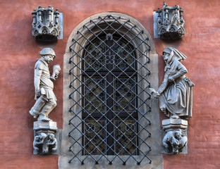 Detail on the wall of the Town Hall in Wroclaw, Poland, above the entrance to Piwnica Swidnicka: a sculpture of a drunk farmer returning back home and his furious wife, holding a clog in her hand. - obrazy, fototapety, plakaty